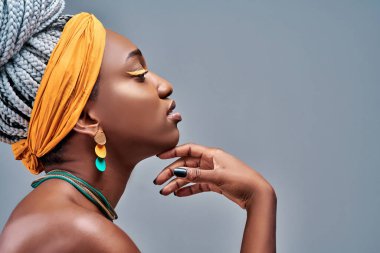 Afro-Amerikan kadın profili. Çıplak, şehvetli, kendine güvenen, çekici, çekici, güzel bir portre. Mükemmel teninin tadını çıkartıyor, parmaklarıyla boynuna dokunuyor, gri arka planda soyutlanıyor.