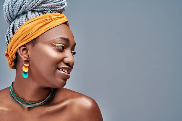 Side view of young fashion african woman wearing yellow headscarf on grey background. Copy space
