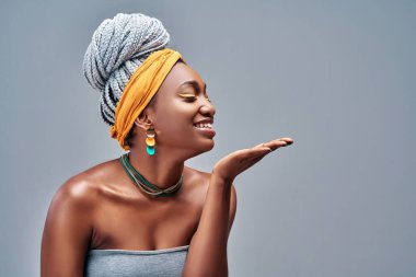 Gri arka planda açık avuç içinden hava öpücüğü veren Afro-Amerikan kadın portresi. Boşluğu kopyala