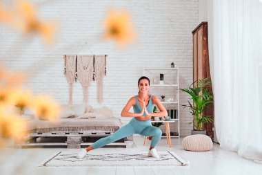 Mavi spor sutyen ve tayt giyen sporcu bayan sporcu evde çömelme egzersizi yapıyor. Seçici odak