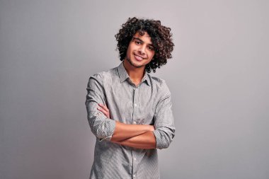 Elleri çapraz olan, gri duvarın karşısında gülümseyen, kameraya bakan gündelik giysiler giymiş genç modern Arap öğrenci. İzole edilmiş gri arka plandaki Hintli adam