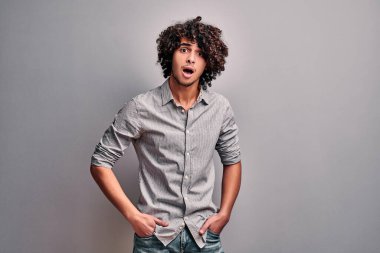 Kıvırcık saçlı doğulu genç adamın stüdyo görüntüsü. Gri arka planda rahat giyinmiş heyecanlı Hintli öğrenci
