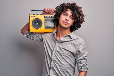 Omzunda sarı retro stereo çalan yakışıklı doğu delikanlının stüdyo fotoğrafı. Gri arka planda müzik kutusuna sahip öğrenci