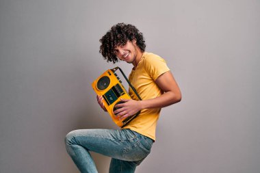 Heyecanlı gülümseyen Arap çocuk, sarı tişörtlü ve kot pantolonlu, eski moda stereo çalan, izole edilmiş gri arka planda dans eden.