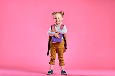 Not defterleri ve sırt çantalı ilkokul kızı pembe arka planda izole edilmiş. Boşluğu kopyala