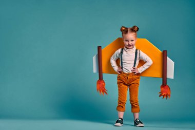 Oyuncak karton uçak kanatlarıyla mutlu, güzel, komik küçük kız gülüşü, stüdyo çekimi izole edilmiş mavi arka plan. Özgürlük kavramını başlat. Boşluğu kopyala