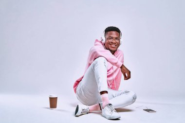 Çekici, akıllı genç bir adam stüdyoda yerde oturmuş kulaklık ve cep telefonuyla müzik dinliyor. Boşluğu kopyala