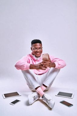 Genç afro adam yerde oturuyor ve beyaz arka planda bir sürü alet kullanıyor. Dikey fotoğraf
