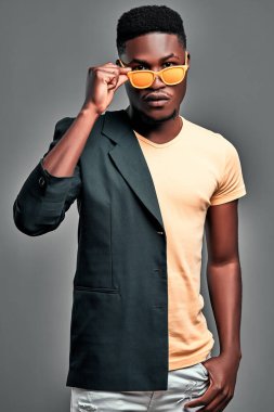 Adam parti için hazır. Omzunda parlak güneş gözlüğü olan, gri arka planda ceketli bir afro adam. Dikey fotoğraf