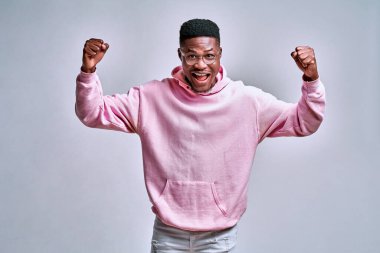Pembe kapüşonlu genç Afro-Amerikalı adam, yumruklarını kaldırdı, havalı olduğumu söyledi ve gri arka planda durup gülümsedi..