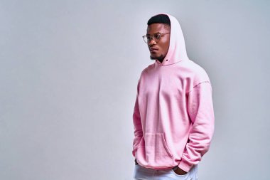 Stüdyoda açık kırmızı arka planda pembe kapüşonlu Afro-Amerikan bir adamın resmi çekildi. Moda ve yaşam tarzı.