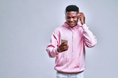 Yakışıklı Afro-Amerikalı adam beyaz kulaklık takıyor ve telefondan müzik dinliyor. Müzik, duygu ve yaşam tarzı kavramı. Boşluğu kopyala.