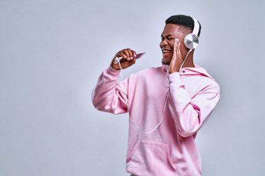 Yakışıklı Afro-Amerikan erkeği beyaz kulaklıklarla en sevdiği müziği dinlemeyi ve şarkı söylemeyi sever. Müzik konsepti, duygular ve ifadeler.