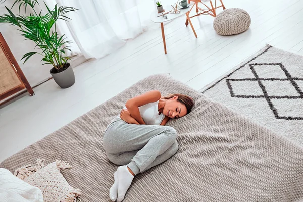 Adet sancısı çeken karnını tutarak acı çeken genç ve güzel bir kadın kanepeye uzanmış, kadın sağlığı konseptinde karın krampı yaşıyor. Üst görünüm