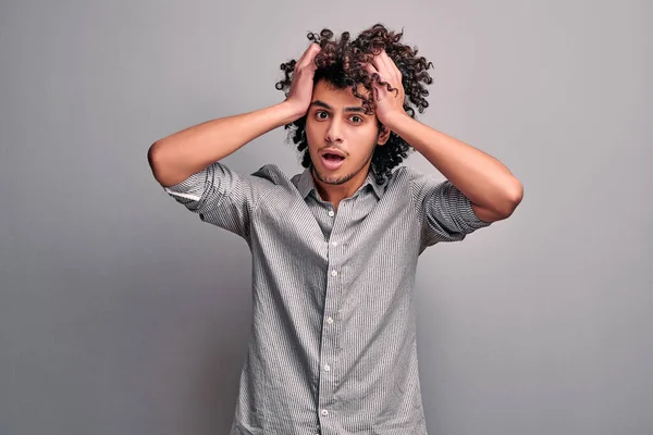 Waist up studio portrait of muslim young man clasping his curly head. Stressed student on isolated gray background