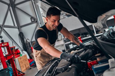 Tamirhanesinde araba tamircisi arabanın yanında duruyor. Motorun yakın görüntüsü.