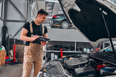 Mekanik bir araba motorunu kontrol ediyor ve not alıyor. Seçici odak.