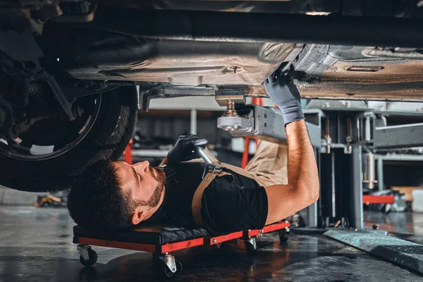 专心致志的汽车修理工在地板上单独工作 修理汽车底部 看细节 排除汽车故障 有选择的重点 — 图库照片
