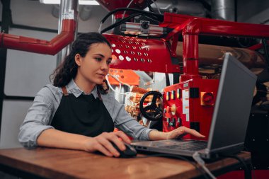 Modern kahve kızartma makinesini çalıştıran bir kadın bilgisayarını kontrol ediyor..