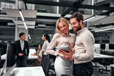 Two handsome business people communicate together and look at the tablet screen standing in a spacious office. The concept of business, finance, projects, teamwork.