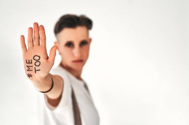 Young woman making stop gesture against white background, focus on hand. Metoo hashtag word on palm. Victim of sexual assault and harassment. Copy space. Isolated white background.
