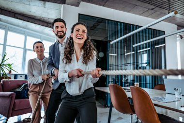 Bir grup gülümseyen ofis çalışanı halat çekme oyunu oynuyorlar. İş avantajı kavramı