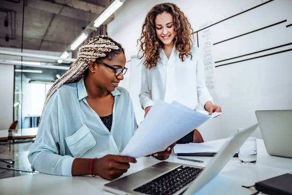 Two young women work together in a bright office. Work on the project, consultation.