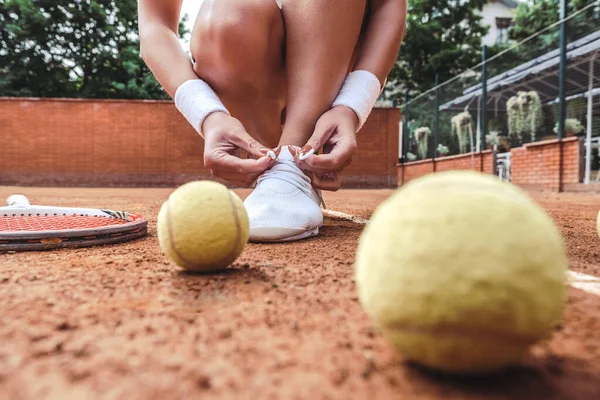 テニスコートで靴ひもを結ぶテニスプレーヤーのビューを閉じます スポーツクラブのテニスコートの若い女性 — ストック写真