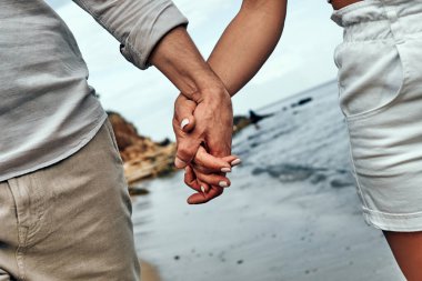 Couple holding hands together at the beach. Cropped photo. Close up view