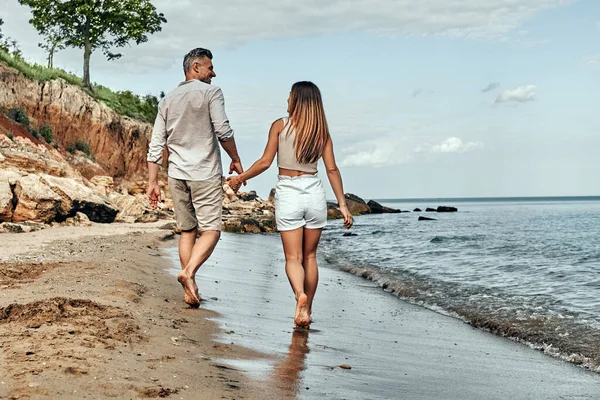 Back view of happy middle aged couple walking on a deserted beach. Full length. Copy space