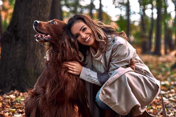 Beautiful woman hugging her pet in the autumn park. A beautiful brown purebred dog looks away.