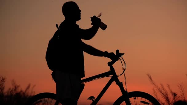 Ciclista bebe agua de su cantimplora, silueta al atardecer — Vídeos de Stock