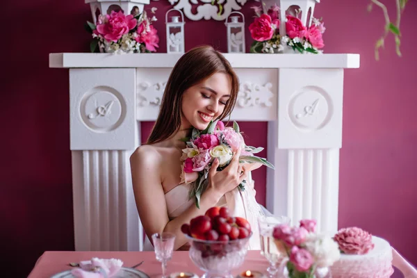 Junge schöne Braut mit einem Strauß rosa Pfingstrose in der Nähe des weißen Kamins — Stockfoto