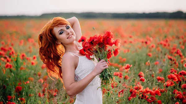 Красивая молодая рыжая женщина на маковом поле с букетом маков — стоковое фото