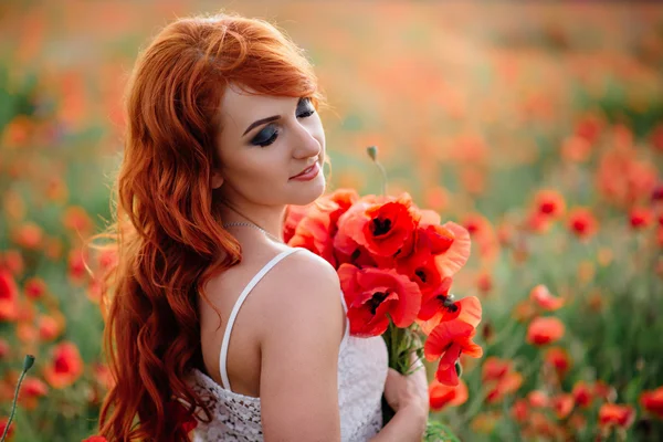 Bela jovem ruiva mulher no campo de papoula segurando um buquê de papoulas — Fotografia de Stock