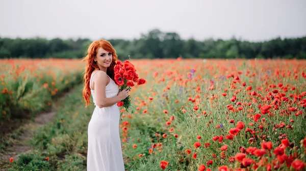 ケシの花の花束を保持にケシ畑で美しい若い赤髪の女 — ストック写真
