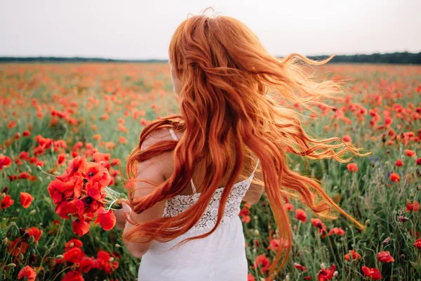 髪に飛んでケシ畑で美しい若い赤髪の女 — ストック写真