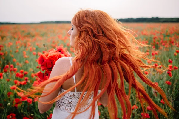 髪に飛んでケシ畑で美しい若い赤髪の女 — ストック写真