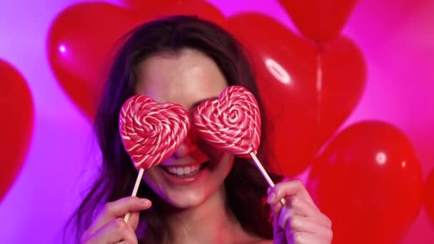 Cheerful young woman with heart shaped lollipops. — Stock Video