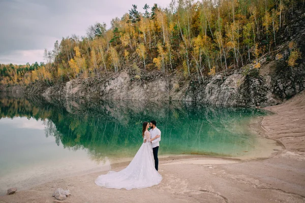 Les jeunes mariés sont debout près d'un beau lac. — Photo