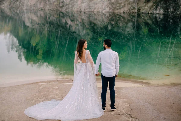 Les jeunes mariés sont debout près d'un beau lac. — Photo