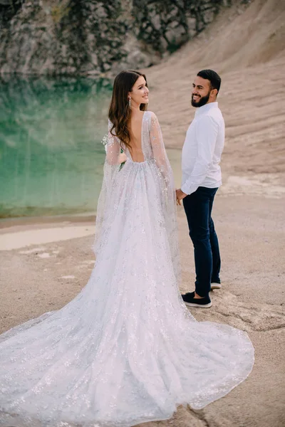 Les jeunes mariés sont debout près d'un beau lac. — Photo