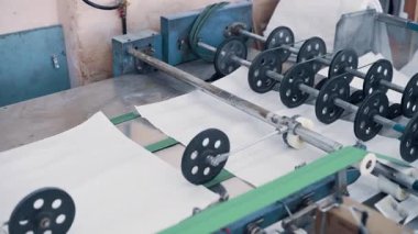 Polipropilen poşet üretimi. Kesik kumaş parçaları taşıyıcı bant boyunca hareket eder ve istiflenir. İşçi süreci izler.