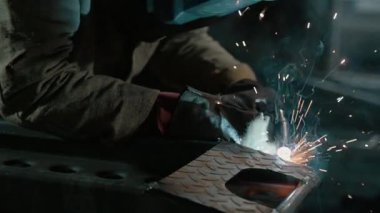 Koruyucu giysiler içindeki kaynakçı atölyedeki metal parçaları kaynaklıyor. Yavaş çekim.