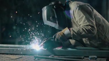 Koruyucu giysiler içindeki kaynakçı atölyedeki metal parçaları kaynaklıyor. Yavaş çekim.