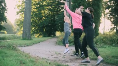 Parkta spor yapan üç orta yaşlı kız arkadaş. Spor kıyafetleri içinde bir grup kadın sabah ısınması yapıyor..