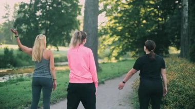 Parkta spor yapan üç orta yaşlı kız arkadaş. Spor kıyafetleri içinde bir grup kadın sabah ısınması yapıyor..