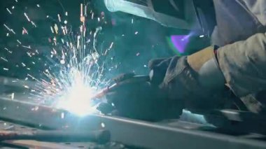 Meşale endüstriyel bir tezgahta çeliği kaynatırken parlak kıvılcımlar uçuşan kaynak yapan bir işçinin yakın çekimi. Yavaş çekim.