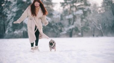 Kar köpeğiyle kış parkında karlı ağaçların arkasında koşan mutlu genç kadın. Yavaş çekim.