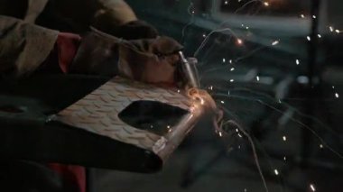 Meşale endüstriyel bir tezgahta çeliği kaynatırken parlak kıvılcımlar uçuşan kaynak yapan bir işçinin yakın çekimi. Yavaş çekim.
